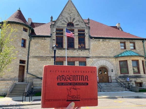 Marguerite Henry Pictured Geography Books Argentina held in front of DuPage County Historical Museum